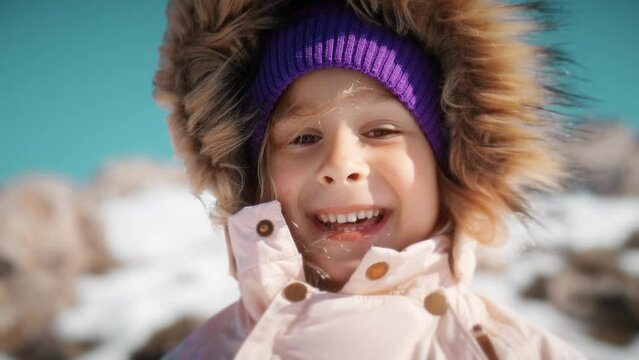 Close-up portrait of a beautiful little girl wearing warm clothes in snowy mountains in winter