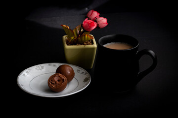 mug of coffee on black background and next to it a snack of chocolate.