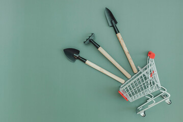 Three gardening tools and a shopping trolley on green.