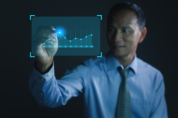 Businessman holding a pen and showing a growing virtual hologram of statistics, graph and chart with arrow up on the dark background. Stock market. Business growth.