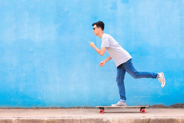 Man skateboarding on  street sidewalk with blue wall in background