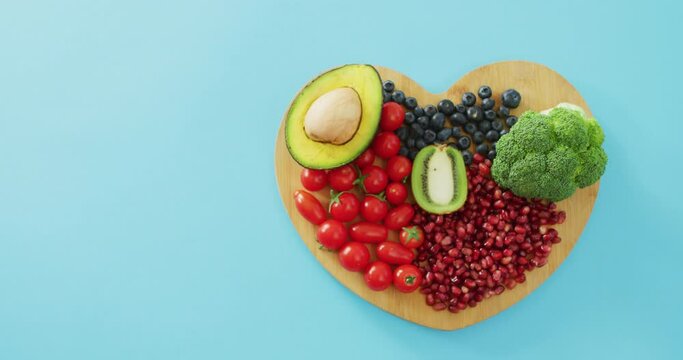 Video of fresh fruit and vegetables with copy space on heart shaped wooden board on blue background