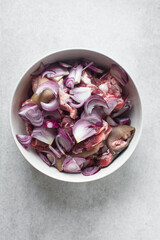 Sliced onions and Fresh raw goat meat in a white bowl, chopped onions and goat meat being prepared for cooking