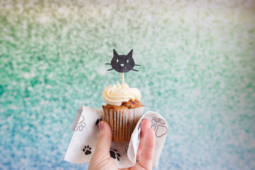 Hand holding a cupcake with a decorative black cat pick