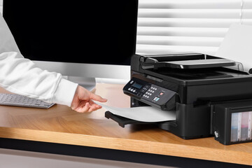 Woman loading paper into printer at wooden table indoors, closeup