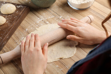 Woman rolling dough for chebureki at wooden table, closeup