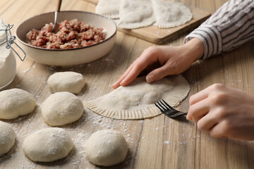 Woman making chebureki with tasty filling at wooden table, closeup
