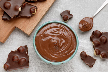 Chocolate pieces and bowl of sweet paste on grey table, flat lay
