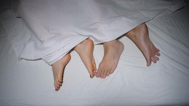 Closeup of legs on white bed sheets.Female and man under the blanket