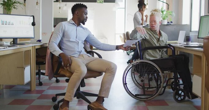 Diverse business people discussing with disabled colleague and documents in creative office