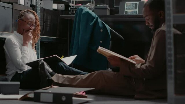 Police Officers Team Examining Case Files Records, Sitting On The Floor Checking Surveillance Photos Of Suspect In Evidence Room. Detectives Trying To Finish Criminal Investigation. Handheld Shot.