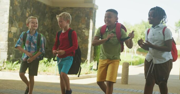 Video of happy diverse boys walking and talking in front of school