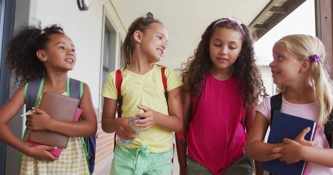 Video of happy diverse girls walking at school corridor and talking