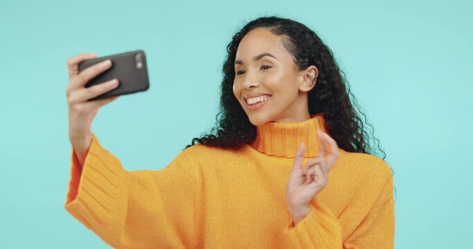 Selfie, pose and black woman with phone in studio, hand gesture and peace sign for social media post. Smile, posing and happy fashion influencer taking profile picture and isolated on blue background