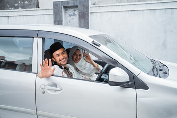 Asian Muslim husband and wife smiling by waving from the car window during Lebaran homecoming trip