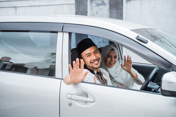 Asian Muslim couple smiling by waving from the car window during Lebaran homecoming trip