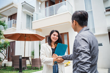 Asian female real estate agent carrying a clipboard while shaking hands with a buyer in a...