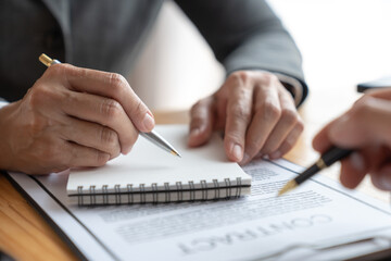 Obraz premium Young Asian lawyer or legal advisor explaining details of business contract agreement with investor taking notes for review and analysis in joining business in office real estate project.