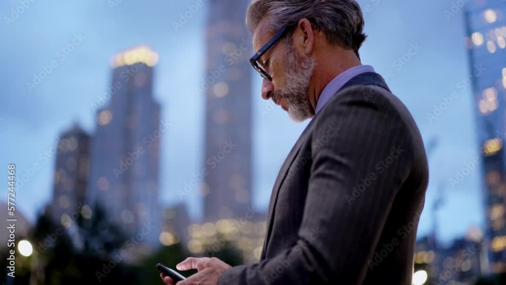 Poster mature successful male in suit and stylish eye glasses reading text message on mobile phone device w
