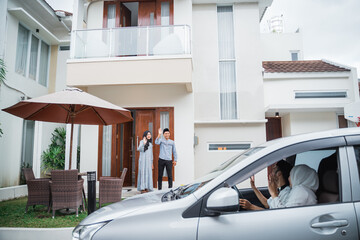 Asian Muslim couple waving to guests arriving by car at home