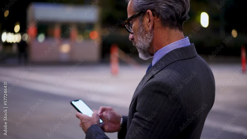 Poster mature successful man in suit and stylish eye glasses typing text message on mobile phone device whi