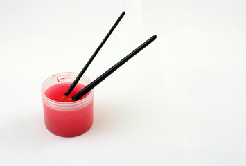 Cleaning red acrylic paint from paintbrushes by soaking in small container filled with water