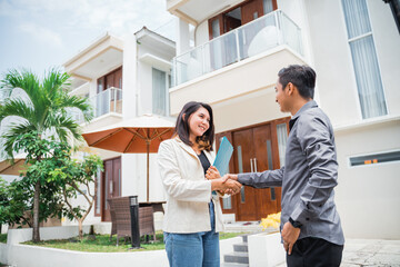 Asian female real estate agent shakes hands with prospective buyers in a residential background