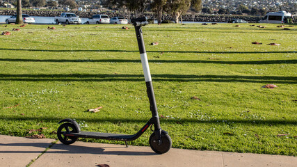 Electric scooter for rent, parked on the side of park's walkway in San Diego, California.