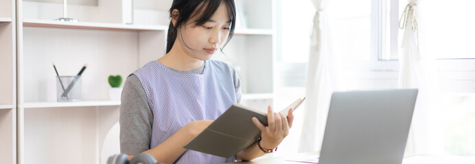 Asian woman taking notes in notebook while studying online in laptop at home, Video chat, Online communication , Stay home, New normal, Distance learning., Social distancing, Learn online..