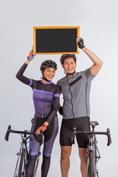 asian couple in cycling outfir holding the blackboard up while standing beside their bicycles on isolated background