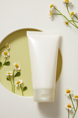 Top view of white plastic tube for facial moisturizer cream or facial cleanser and fresh feverfew on white podium. Mockup for product has ingredients from feverfew, rich in vitamins A and E.