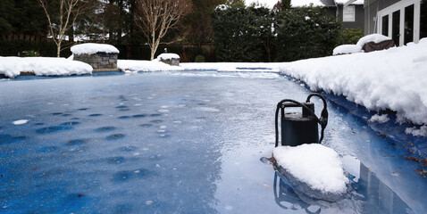 Automatic pool pump in ice and slush after snow storm. Inground backyard pool with black pool pump submerged in deep frozen water. Winterizing pool for cold or freezing temperature. Selective focus.