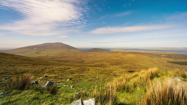 Timelapse of remote village bogland with grass and rocks with clouds casting shadows in daylight viewed from Minaugn Heights in Achill Island in county Mayo in Ireland.