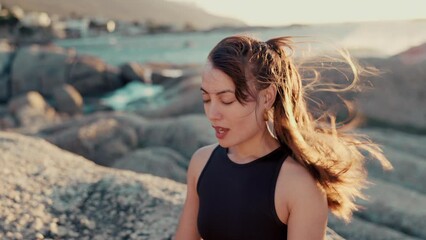 Meditation, peace and relax with woman at beach for spiritual, mindfulness and fitness. Wellness, freedom and windy with girl breathing on rocks in nature for faith, summer break and calm mindset