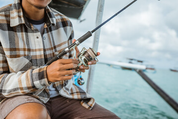 close up of angler's hand checking reel while holding fishing rod on small fishing boat