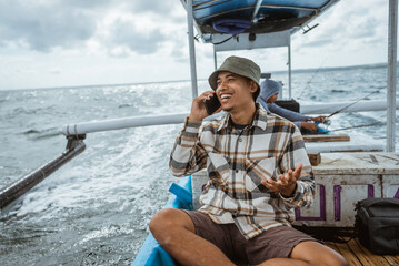 angler receives a cell phone call while sitting on a fishing boat at sea