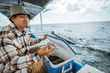 angler disappointed while taking a small bait fish in the box while fishing at sea using a small fishing boat