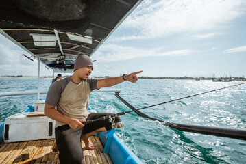 angler with finger pointing while holding rod over a small fishing boat