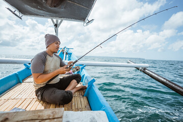 Obraz premium Asian fishermen holding fishing rods while casting on a small fishing boat at sea
