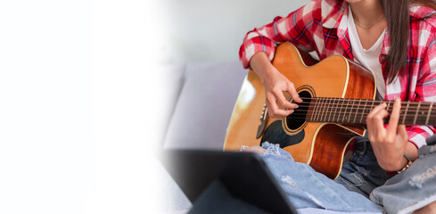 Banner with blank copyspace, Concept of relaxation with music, Young woman plays acoustic guitar while learning music on tablet - obrazy, fototapety, plakaty