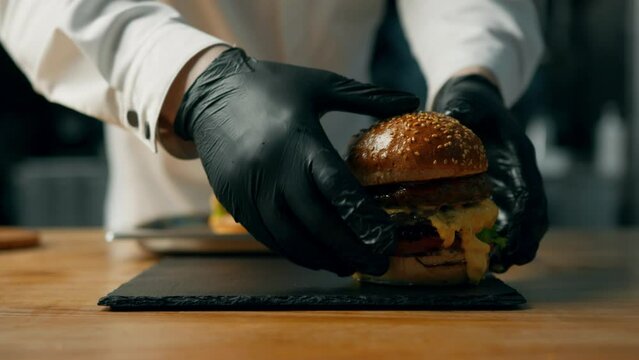 professional kitchen: the chef is checking out burger by adding ingredients.