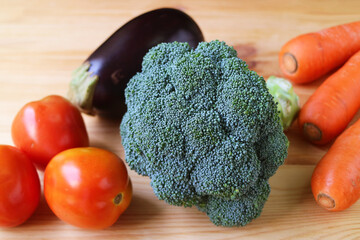 Closeup of raw broccoli with tomatoes, carrots and eggplant on wooden background