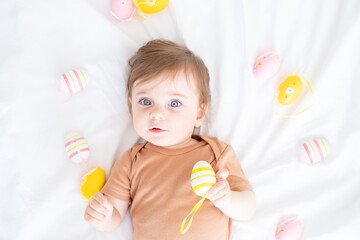 top view of cute funny baby with colorful Easter eggs on bed at home