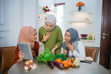 three veiled women surprised to see a tablet while cooking in the kitchen