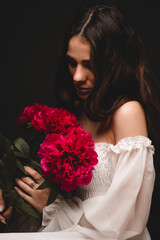 portrait of a young, beautiful and sensual woman with a lush bouquet of red peonies in her hands
