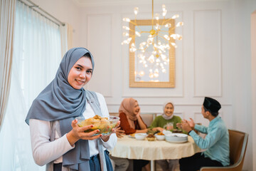 Beautiful veiled girl carrying a plate of food. The muslim family together enjoy the iftar meal in...