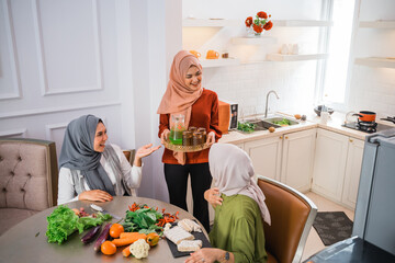 happy friend serving fresh drink for her friend at the kitchen during cooking for dinner