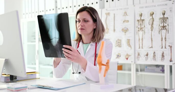Traumatologist examines x-ray and legs and model of knee joint
