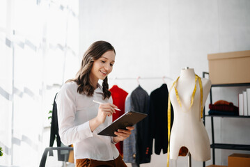 Fashion designer woman talking smart phone and using laptop with digital tablet computer in modern studio in morning light.