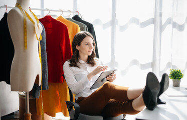 Fashion designer woman talking smart phone and using laptop with digital tablet computer in modern studio in morning light.